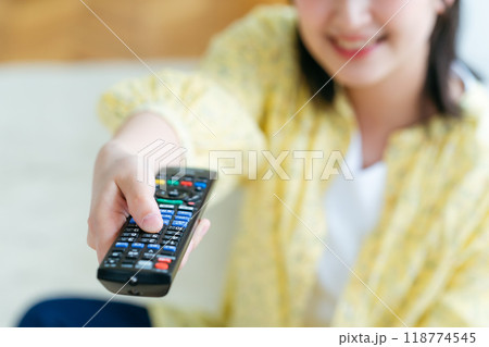 リビングでテレビリモコンを操作する若い女性 118774545