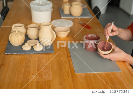 Close-up of a potter's hands with a brush painting ceramic dishes.  118775342