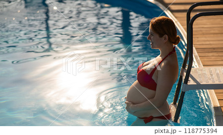 Pregnant red-haired woman in the pool in a red bikini.  118775394