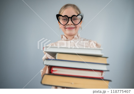 Little girl with glasses holding a stack of books on a white background.  118775407