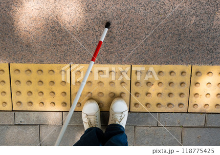 Close-up of female foot, walking stick and tactile tiles. Close-up of female foot, walking stick and tactile tiles. 118775425