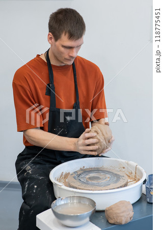 A potter kneads clay before using it on the potter's wheel. Vertical photo. A potter kneads clay before using it on the potter's wheel. Vertical photo. 118775451