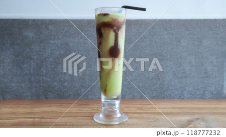 A glass of avocado juice with a little chocolate topping on the table. 118777232