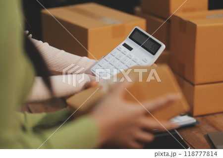 Startup SME small business entrepreneur of freelance Asian woman wearing apron using laptop and box to receive and review orders online to prepare to pack sell to customers, online sme business ideas. Startup SME small business entrepreneur of freelance Asian woman wearing apron using laptop and box to receive and review orders online to prepare to pack sell to customers, online sme business ideas. 118777814