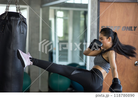 Asian boxing athlete woman kick punching bag by left foot in gym 118780890