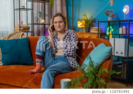 Happy young Caucasian woman making mobile phone conversation with friends sitting on couch at home 118781491