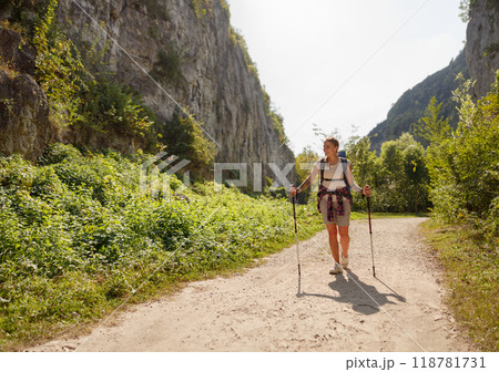 A hiker enjoying a beautiful scenic trail while using walking poles amidst natures beauty A hiker enjoying a beautiful scenic trail while using walking poles amidst natures beauty 118781731