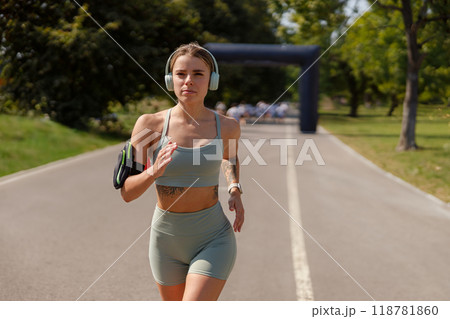 A Young Woman Energetically Running Outdoors While Wearing Headphones in Her Athletic Gear 118781860