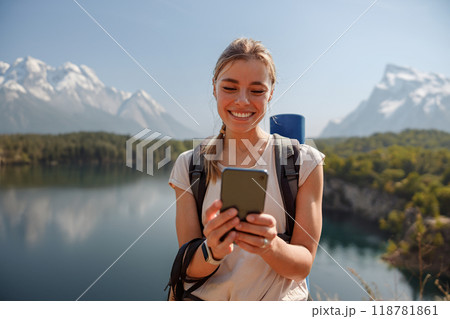 A smiling hiker uses a smartphone while enjoying the beautiful lake and mountains 118781861