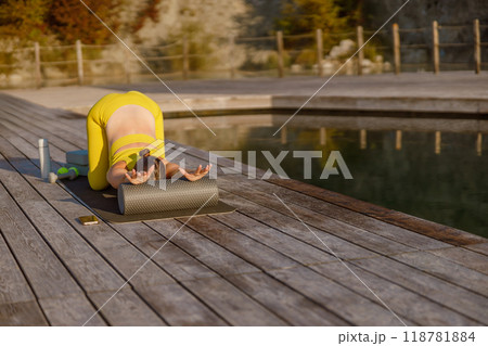 A Woman Engaging in Yoga Practice in the Outdoors Beside a Peaceful and Calm Pool 118781884