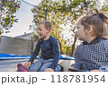 Two children sitting outdoors, smiling and engaging with each other in a playful environment, surrounded by trees and soft lighting 118781954
