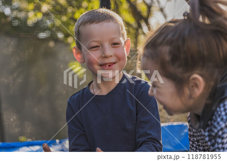 A boy and a girl happily sitting on a trampoline together outdoors 118781955