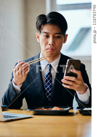 弁当を食べながらスマホを操作する20代の若い男性 118783740