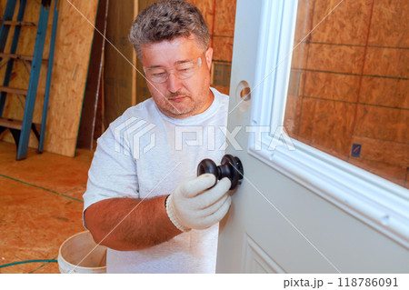 With use of screwdriver, professional locksmith installs lock doorknob on front door of home With use of screwdriver, professional locksmith installs lock doorknob on front door of home 118786091