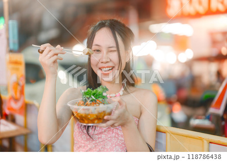 Asian foodie tourist woman eating spicy grilled squid at China town asia street food night market 118786438