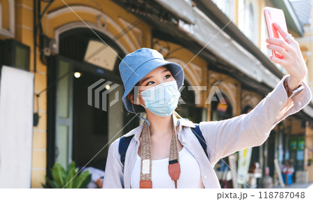 Young adult asian woman backpack traveller wear hat and face mask for covid-19 using mobile phone for selfie Young adult asian woman backpack traveller wear hat and face mask for covid-19 using mobile phone for selfie 118787048