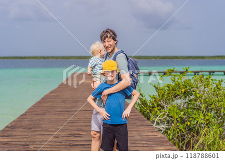 Father with his toddler and teenage sons exploring wooden pier over the turquoise waters of Bacalar Lake, Mexico. Peaceful tropical travel destination concept 118788601