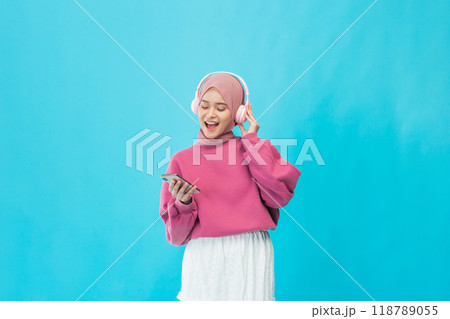A young woman enjoys her favorite music with headphones against a vibrant blue background 118789055