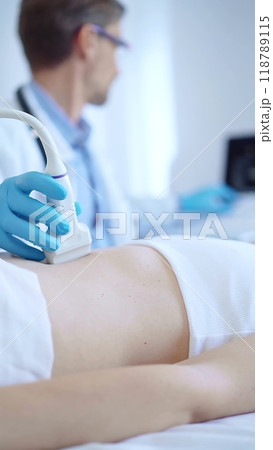 Doctor man wearing a blue protective gloves using an ultrasound machine on a female patient examining internal organs. Medicine concept Doctor man wearing a blue protective gloves using an ultrasound machine on a female patient examining internal organs. Medicine concept 118789115