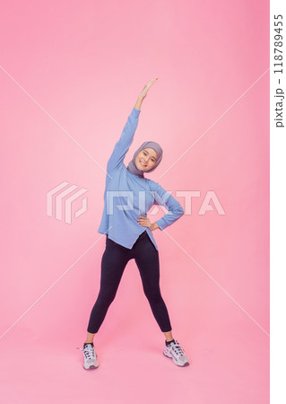 An Active Young Woman Joyfully Stretching Her Body Against a Vibrant Pink Background Displaying Her Enthusiasm An Active Young Woman Joyfully Stretching Her Body Against a Vibrant Pink Background Displaying Her Enthusiasm 118789455