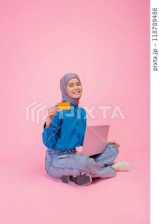 A Young Woman in Hijab Enthusiastically Shopping Online with Her Credit Card Against a Pink Background A Young Woman in Hijab Enthusiastically Shopping Online with Her Credit Card Against a Pink Background 118789486