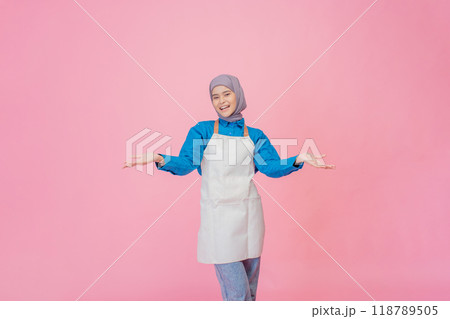 A Cheerful and Young Woman Wearing an Apron Poses Against a Pink Background 118789505