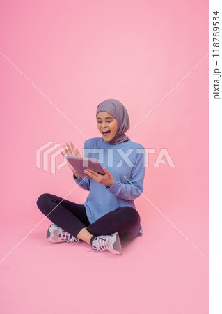 Happy Young Woman using a Tablet on a Bright Pink Background in Casual Outfit Happy Young Woman using a Tablet on a Bright Pink Background in Casual Outfit 118789534