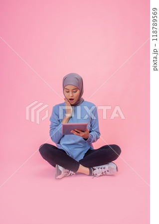 A Young Woman Actively Engaged with Her Tablet Against a Vibrant Pink Background 118789569