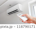 Air conditioner temperature adjustment with remote controller in room at home. Hand holding remote controller of air conditioner inside the white room and set at cool temperature 118790171