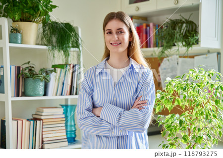 Portrait of smiling female teenager looking at camera with crossed arms in home 118793275