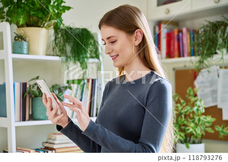Happy female teenager using smartphone, standing at home 118793276