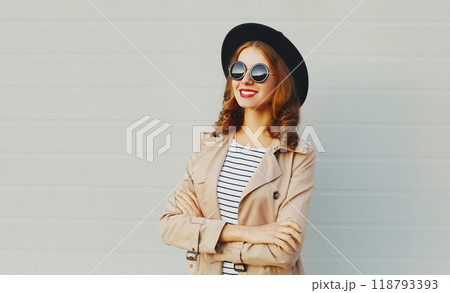 Fashion portrait happy woman with crossed arms wearing a black hat sunglasses over grey background 118793393