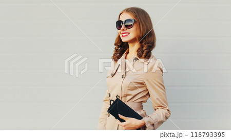 Fashion pretty smiling woman model wearing a coat and black handbag clutch over grey background 118793395