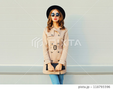 Fashion pretty woman model wearing a black hat coat and handbag posing over grey background 118793396