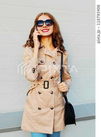 Happy beautiful young woman talking on smartphone standing on grey background Happy beautiful young woman talking on smartphone standing on grey background 118793406