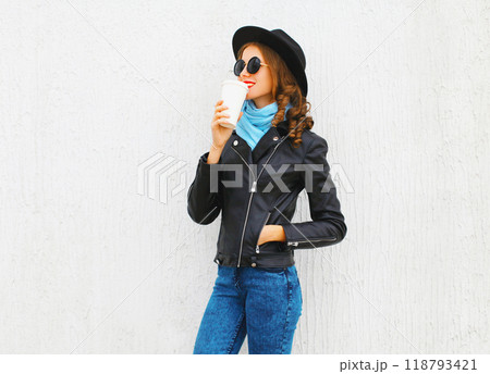Fashion cool girl drinks coffee from cup wearing black rock jacket, hat over white background Fashion cool girl drinks coffee from cup wearing black rock jacket, hat over white background 118793421