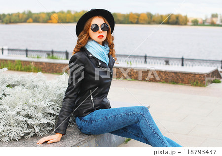 Fashion young woman posing in black rock jacket, hat at city park 118793437