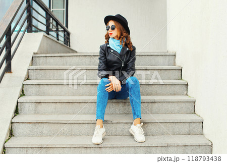Fashion portrait pretty young woman wearing a black rock jacket and hat sitting in city Fashion portrait pretty young woman wearing a black rock jacket and hat sitting in city 118793438