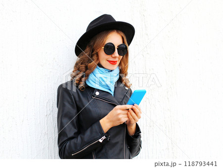 Fashion young woman using smartphone wearing a black rock jacket hat over white background 118793441
