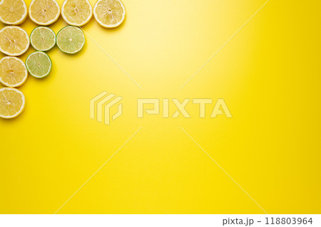 Freshly cut slices of lemons and limes on the left upper corner of the image on a yellow background. 118803964