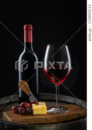 A glass of red wine with a bottle of cheese and grapes on an old wine barrel A glass of red wine with a bottle of cheese and grapes on an old wine barrel 118804212