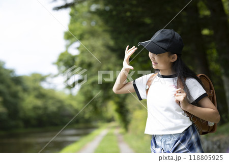 田舎の通学路の森の中を歩く、ランドセルを背負った、下校中の小学生の女の子 田舎の通学路の森の中を歩く、ランドセルを背負った、下校中の小学生の女の子 118805925