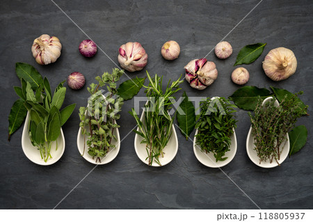 Fresh herbs in porcelain bowls, bay leaves and fresh garlic on a large slate plate 118805937