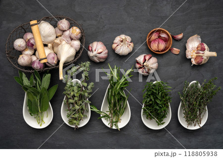 Herbs in porcelain bowls, fresh garlic bulbs in a metal basket 118805938