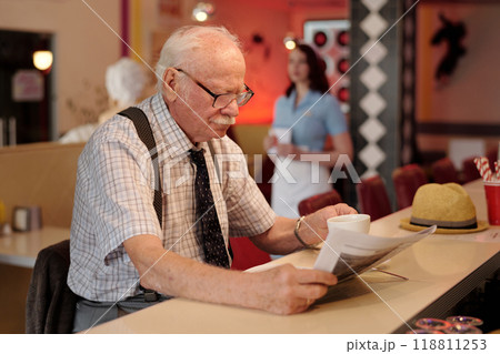 Elderly Man Reading Newspaper in Cozy Coffee Shop Elderly Man Reading Newspaper in Cozy Coffee Shop 118811253