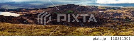 A panoramic view of a rocky, mountainous Irish landscape. In the foreground, a field of brown, yellow, and green grasses. The background features a distant, rolling hills. A panoramic view of a rocky, mountainous Irish landscape. In the foreground, a field of brown, yellow, and green grasses. The background features a distant, rolling hills. 118811501