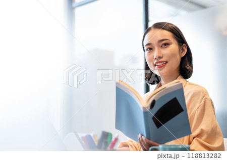 参考書を片手に笑みを浮かべてコチラを見る女性 118813282
