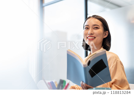 本を片手にパソコン作業しながら笑顔を見せる女性 118813284