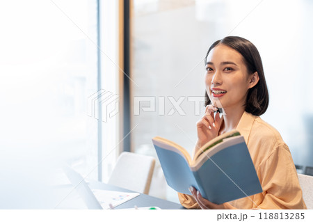 本を片手にパソコン作業しながら笑顔を見せる女性 118813285