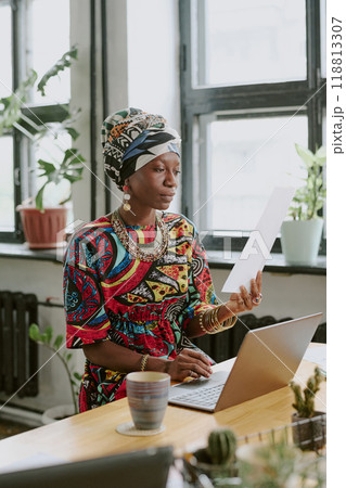 Vertical shot of African American woman sitting at work desk and reading report in modern office Vertical shot of African American woman sitting at work desk and reading report in modern office 118813307